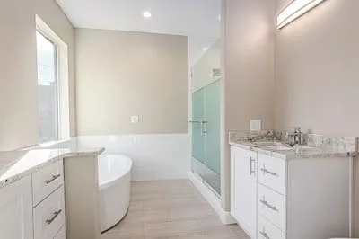 Master bathroom with white cabinetry, marble counters, freestanding tub, and glass shower