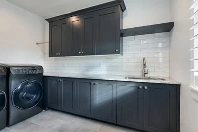 Dark cabinetry with white subway tile backsplash in laundry room with concrete floor