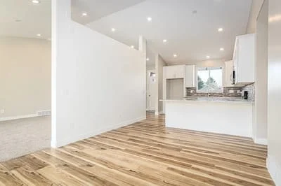 Open concept kitchen and living room with hardwood floors, white walls, recessed lighting, and modern white cabinetry