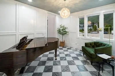 Music room with white wall paneling, black piano, checkered marble floor, and modern pendant lighting