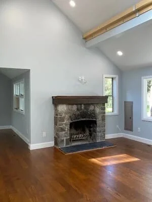 Interior room with white and blue painted walls, stone fireplace, wood floors, and exposed beam ceiling