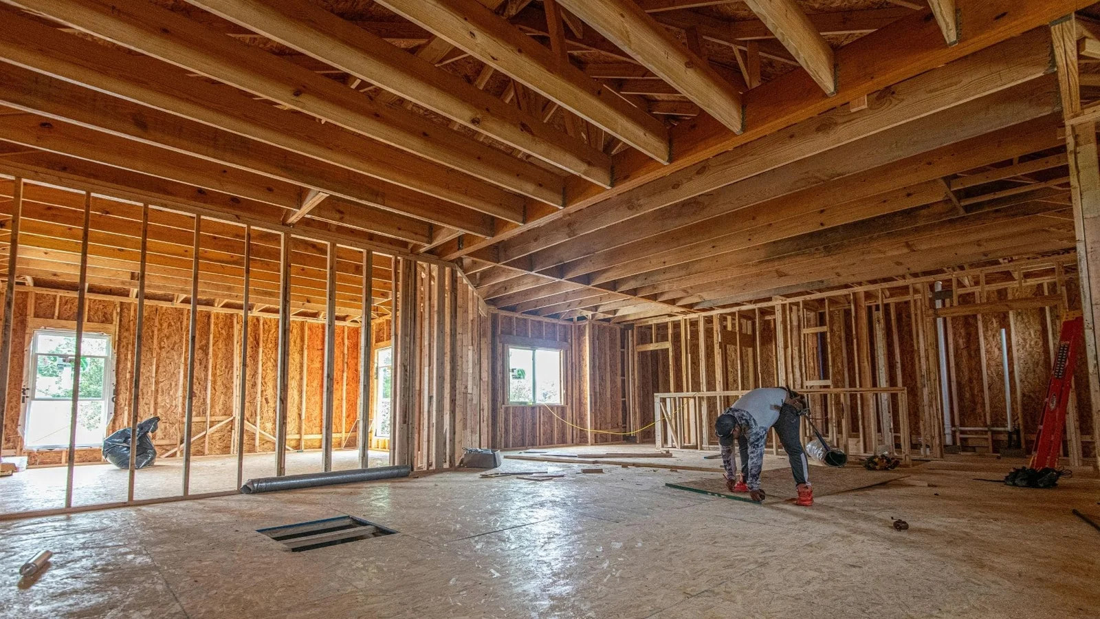 Interior framing with exposed beams, stud walls, concrete floor, and large windows during construction phase