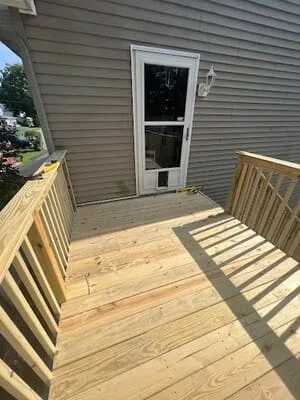 Newly constructed pressure-treated wood deck with railings and balusters attached to house