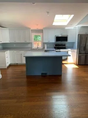 Kitchen with white cabinets, blue island, stainless appliances, and hardwood floors